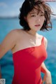 A woman in a red one piece swimsuit standing in the water.