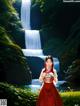 A woman in a red dress standing in front of a waterfall.