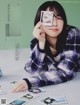 A woman sitting at a table holding a polaroid in front of her face.