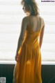 A woman in a yellow dress standing by a window.