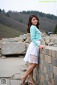 A woman leaning against a stone wall in a white dress.