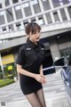 A woman in a black dress standing next to a car.