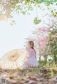 A woman in a pink kimono sitting under a tree holding an umbrella.