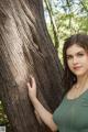 A woman leaning against a tree in the woods.