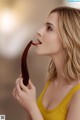 A woman in a yellow tank top holding a chocolate banana.