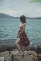 A naked woman standing on a rock by the ocean.