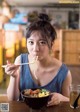 A woman sitting at a table eating a bowl of noodles.