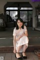 A woman in a white dress sitting on a wooden floor.